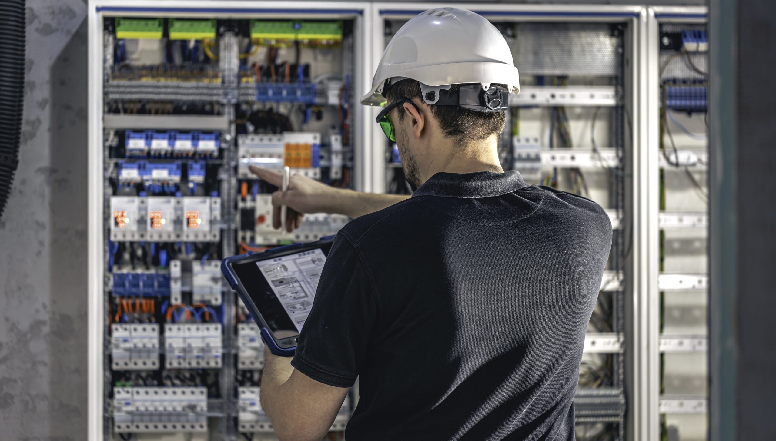 Home man, an electrical working in a switchboard with fuses, uses a tablet.